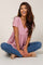 woman wearing a pink dotted short sleeve top with a gathered waist, sitting cross-legged and smiling