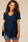 woman with curly hair wearing a navy blue swiss dot maternity top and denim shorts