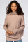 woman wearing a light brown oversized sweater with a cowl neck and long sleeves, paired with blue jeans