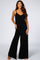 woman wearing a black sleeveless jumpsuit with wide legs and pockets, smiling at the camera