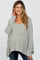 woman wearing a light gray oversized maternity sweater with a v-neck and long sleeves, smiling at the camera