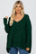 woman wearing a loose-fitting green knitted sweater with a v-neck and long sleeves, paired with blue jeans