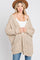 woman wearing a beige oversized knit cardigan with pockets and a white tank top, styled with a brown hat