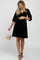 woman wearing a black velvet maternity dress with a baby bump, holding a small handbag and standing gracefully