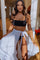 woman wearing a black crop top and a white sheer skirt tied at the waist, posing in a bright indoor setting