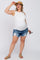 Smiling pregnant woman wearing a white maternity tank top, distressed denim shorts, and a straw visor.