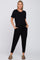 pregnant woman wearing a black short sleeve maternity jumpsuit with pockets and olive green sandals