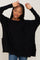 woman wearing a black oversized knit sweater with side pockets and a relaxed fit, smiling while raising her hands