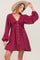 woman wearing a burgundy button-up dress with lace details and long sleeves, accessorized with a wide-brimmed hat