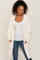 woman wearing a white oversized cardigan over a white tank top and blue jeans, hands in pockets