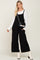 woman wearing a black jumpsuit over a white long sleeve top, paired with white ankle boots and a black handbag