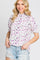 woman wearing a white floral mock neck blouse with purple flowers and distressed denim shorts