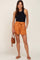 woman wearing black ribbed tank top and orange tie-waist shorts holding a brown leather crossbody bag