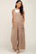 pregnant woman wearing a tan gauze maternity jumpsuit with wide legs and side pockets over a white top