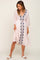 woman wearing a light pink maxi dress with navy blue embroidery and a tie waist detail, styled with white sandals