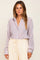 woman wearing a lavender pleated button-down shirt and cream high-waisted trousers