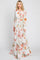 Woman wearing a long sleeve white floral maxi dress with orange and pink flowers and a waist tie