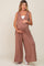 woman wearing a brown sleeveless maternity jumpsuit with a deep v-neck and holding her baby bump