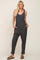 Woman wearing a charcoal grey ribbed sleeveless jumpsuit with pockets and olive green sandals