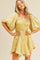 woman wearing a light yellow puff sleeve mini dress with a smocked bodice and a tie waist