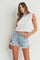 woman wearing a white cropped tank top and light blue distressed denim shorts