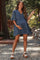 woman wearing a denim blue maternity dress with tiered ruffles and holding her baby bump outdoors