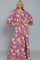 woman wearing a purple floral maxi dress with a deep v-neck and bell sleeves, posing with hands on hips
