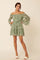 woman wearing a green floral off-shoulder dress with bell sleeves and a ruffled hem, standing against a neutral background