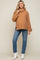Pregnant woman wearing a camel oversized turtleneck sweater, blue jeans, and white ankle boots