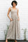 woman wearing a floral maxi dress with ruffle straps and pockets, standing against a white brick wall