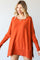 woman wearing a loose-fitting orange oversized sweater with side slits and a round neckline