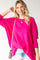 smiling woman wearing a bright pink oversized sweater and gold necklace against a white background