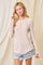Woman wearing a beige long sleeve henley top and distressed denim shorts against a neutral backdrop