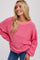 smiling blonde woman wearing a bright pink crewneck sweater and blue jeans