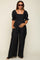 woman wearing a black maternity jumpsuit with puff sleeves and a smocked bodice, holding her baby bump