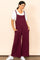 woman wearing a maroon wide-leg jumpsuit with adjustable straps and pockets, paired with a white t-shirt and sneakers