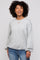 woman wearing a light gray oversized sweater and blue jeans with curly hair and a subtle smile