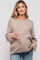 woman wearing a beige maternity sweater with long sleeves and holding sunglasses