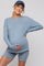 woman wearing a light blue ribbed maternity sweater and matching shorts, gently cradling her baby bump
