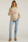 woman wearing a light beige maternity sweater and distressed jeans, holding her baby bump