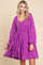 woman wearing a bright purple long sleeve dress with a gathered bodice and flared skirt