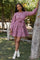 woman wearing a pink tiered dress with long sleeves and a tie waist, standing outdoors by a tree