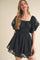 woman wearing a black lace puff sleeve mini dress with a square neckline and a fitted waist
