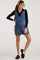 woman wearing a denim maternity overall dress with pockets and a black long sleeve top underneath
