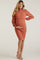 woman wearing a rust ribbed maternity dress with a fitted silhouette and long puff sleeves, holding her baby bump