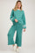 woman wearing a teal maternity wear loungewear set with long sleeves and wide-leg pants, smiling and standing against a neutral background