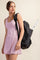 woman wearing a light pink sleeveless athletic dress and carrying a black backpack with a tennis racket peeking out