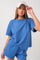 woman wearing a light blue short sleeve textured top and matching shorts, holding a white cap with text