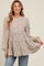 woman wearing a beige maternity top with a leopard print and tiered silhouette, smiling and holding the fabric out