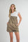 woman wearing a white short sleeve top and khaki overall shorts, striking a playful pose with hands in pockets
